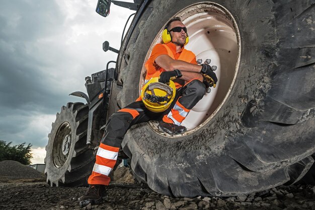 Foto uomo seduto sulla ruota di un veicolo da costruzione