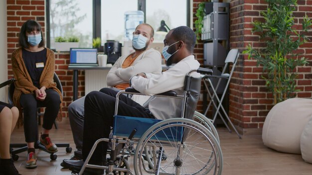 Man sitting in wheelchair and talking about addiction at aa meeting, attending therapy session with group during covid 19 pandemic. Person with disability discussing mental health issues