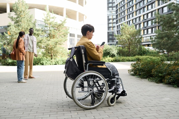 車椅子に座り、街を散歩中にスマートフォンを使用している男性