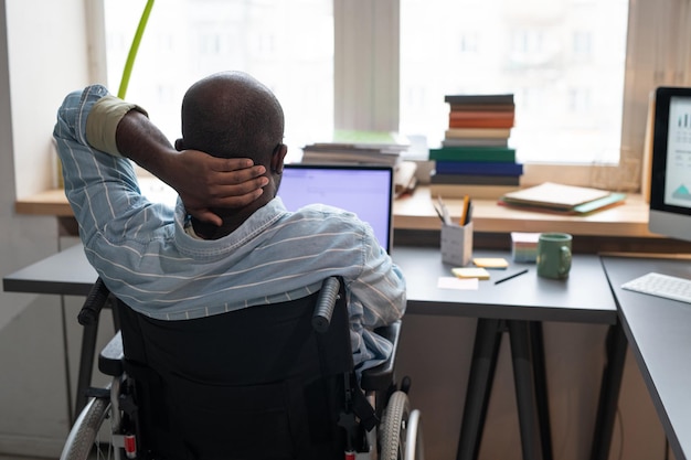 Photo man sitting on wheelchair working on laptop