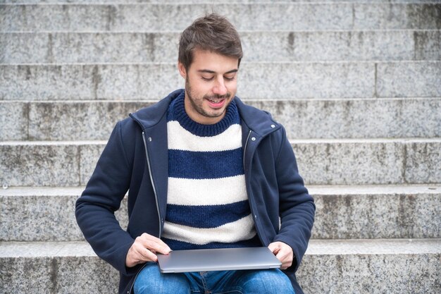 Foto uomo seduto con un laptop sui gradini