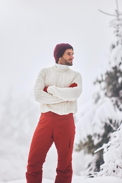 Man in ski suit and sweater in snowy forest during winter vacations outdoors