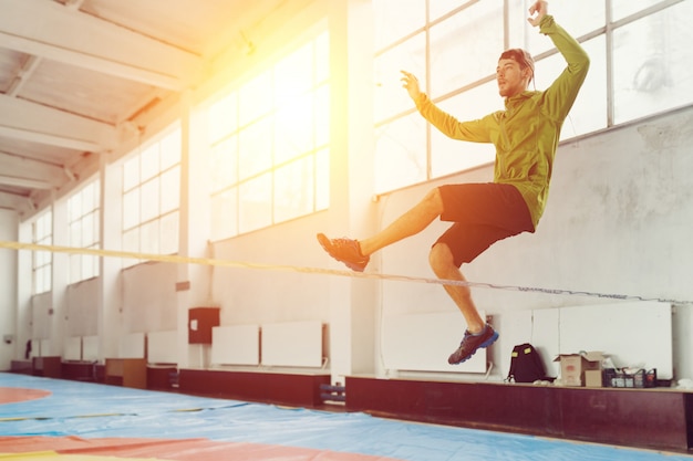 Man slacklining walking and balancing on a rope, slackline in a sports hall