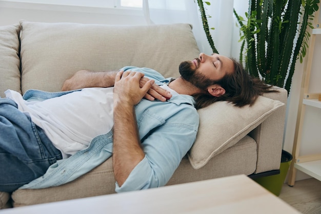 Foto un uomo che dorme sul divano durante il giorno è stanco e rilassato dopo lo stress e si sente male stress sul lavoro sonno scarso e problemi di salute