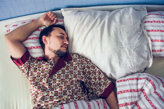 Uomo che dorme nel suo letto sul cuscino bianco