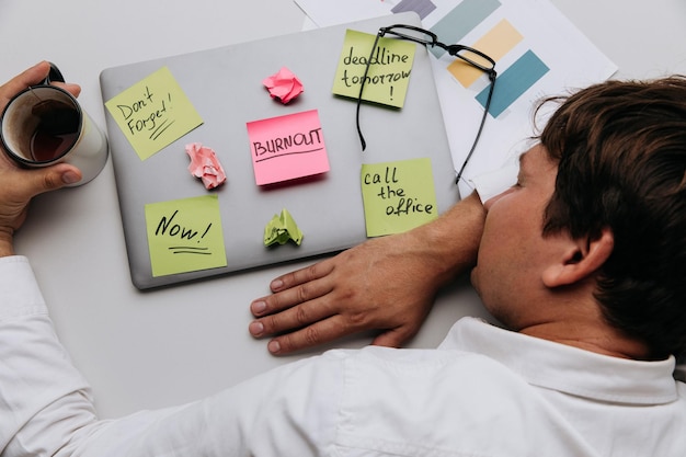 Man sleeps on his desk Worker have sticker pads on his laptop with tasks Top view