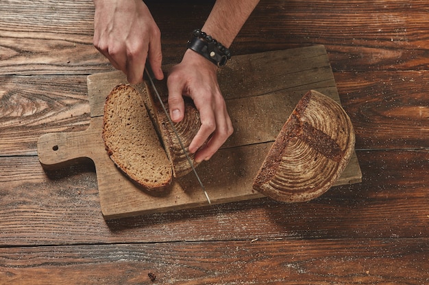 Man slicing freshly baked organic bread on a wooden brown background flat lay