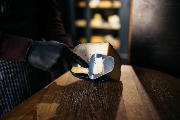 Man slicing a small piece of cheese for taste A young worker uses a special knife for cheese