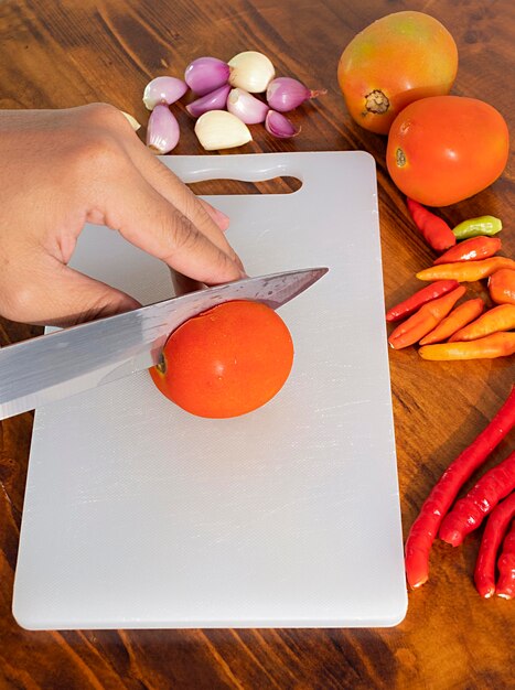 man slicing tomato on wood board