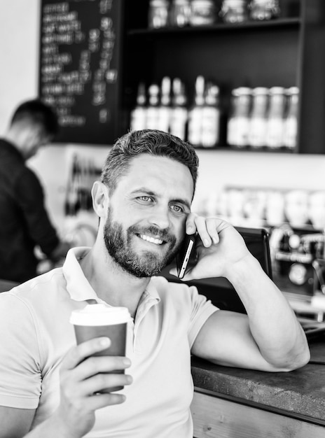 Man smartphone koffie bestellen in café Koffiepauze concept Koffie afhaaloptie voor drukke mensen Man mobiel gesprek café barista achtergrond Drink koffie tijdens het wachten Wachten op je