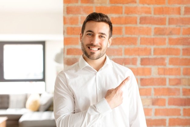 Man smiling cheerfully, feeling happy and pointing to the side and upwards, showing object in copy space