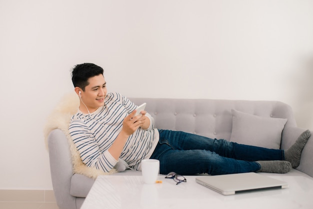 Man smiling reads a text message on his mobile while relaxing at home  in the living room