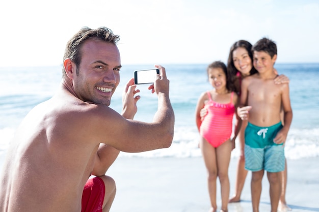 Man smiling while photographing children at sea shore