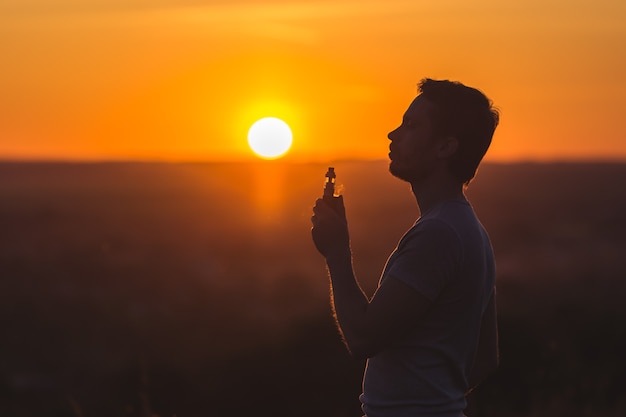 The man smoke an electric cigarette on the background on the sunset