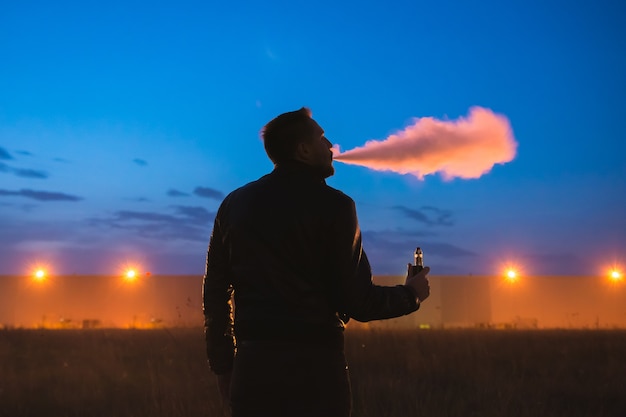 The man smoke electric cigarette near the building. evening night time