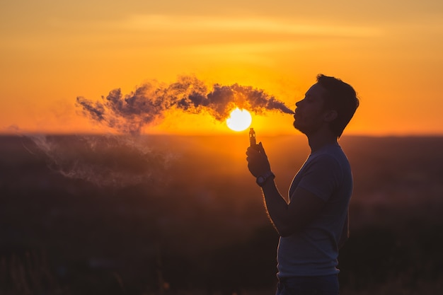 L'uomo fuma una sigaretta elettrica sullo sfondo del tramonto