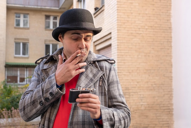 A man smokes a cigarette and drinks alcohol on a city street