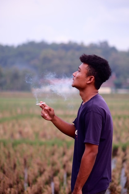 A man smokes a cigarette in a field in indonesia.