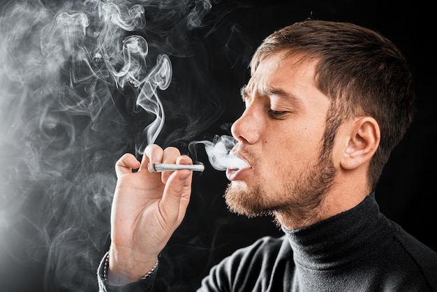 A man smokes a cigarette from a rolled up bill of money