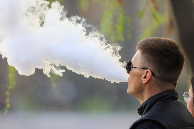 a man smokes an electronic cigarette and blows out smoke