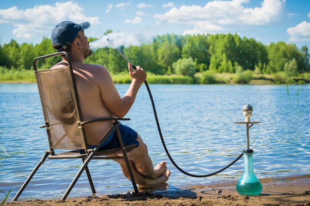 Man smokes a hookah on the river bank