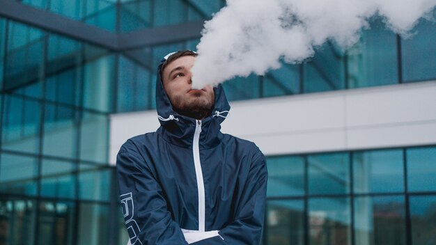 Man smoking electronic cigarette vapor. Smoking Electronic Cigarette against the background of a glass building