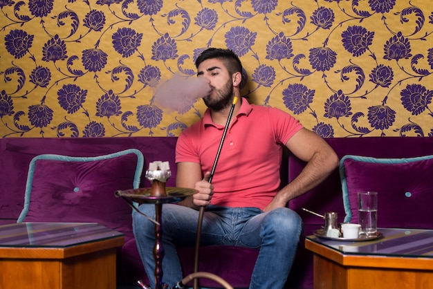 背景にカラフルな壁とカフェでトルコの水ギセル喫煙男