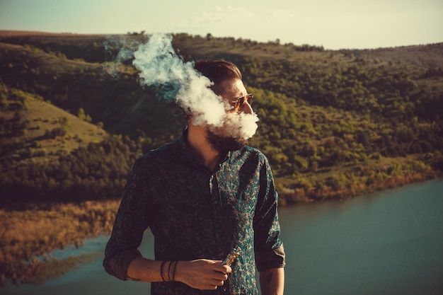 Foto uomo che fuma in piedi vicino al lago.