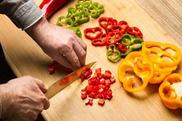 Foto man snijden rode paprika op een houten keukenbord