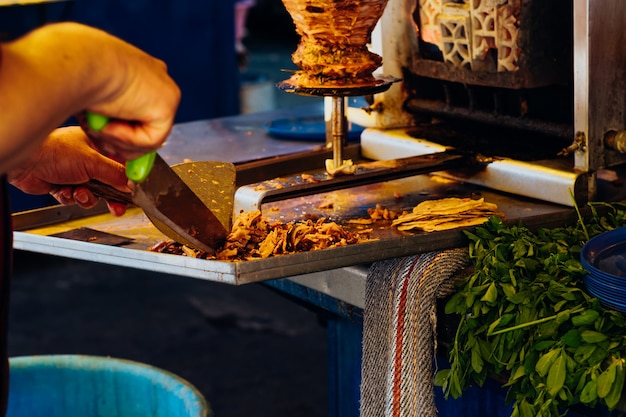 Man snijdt stukken van een stuk vlees in een tol voor taco's al pastor, typisch Mexicaans gerecht.