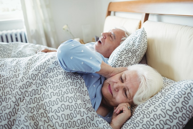 Man snoring and woman covering her ears while sleeping on bed