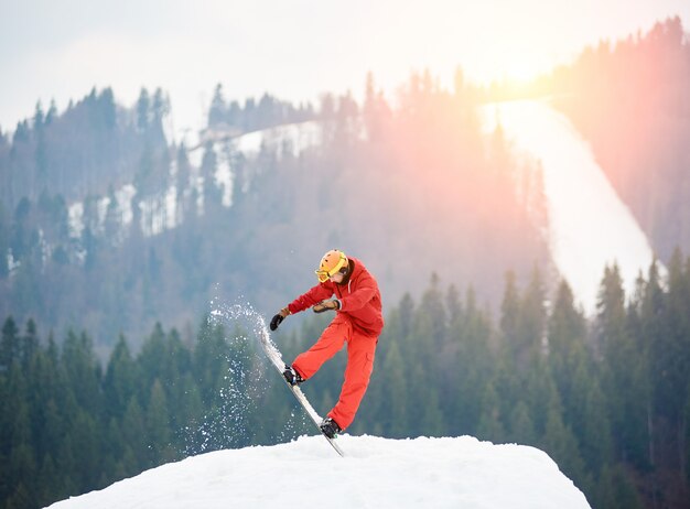 Man snowboarder springen op de top van de besneeuwde heuvel met snowboard in de avond