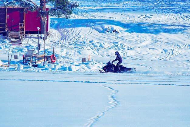 Man at Snowmobile in Winter Finland, Lapland at Christmas. Extreme Sport Activity and Recreation in Cold Season. Drive a Snow Mobile Vehicle. Focus in motion