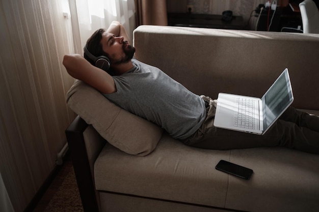 Man on sofa with headphones and notebook at home