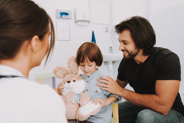 医者のオフィスの子供で男と息子はウサギのおもちゃを保持します。