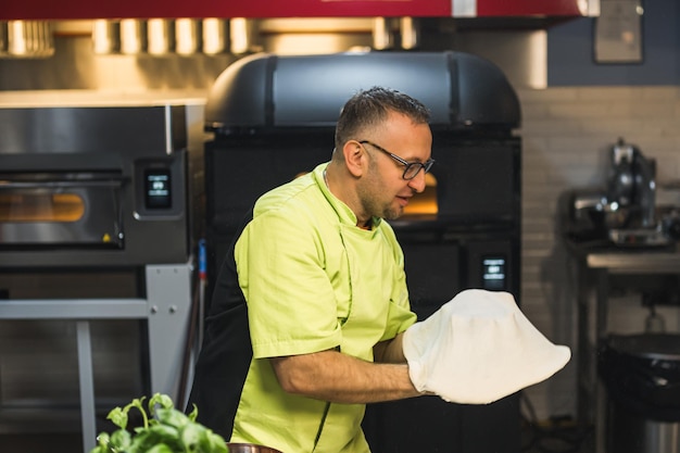 Photo man spinning and tossing pizza dough up in the kitchen