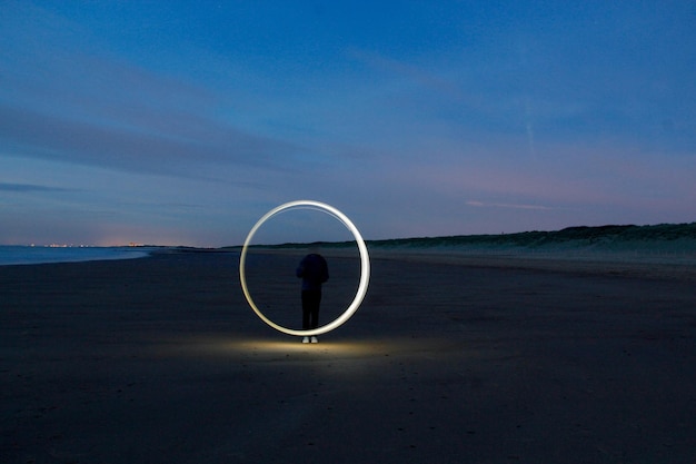 man spinning wire wool at sandy beach against sky during dusk