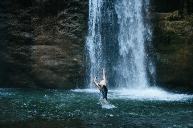 Foto uomo che spruzza acqua mentre salta dalla cascata