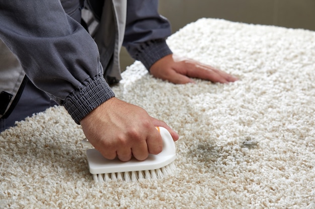 Фото Человек распыляет моющее средство на сером ковре, чтобы удалить пятно в профессиональной уборке