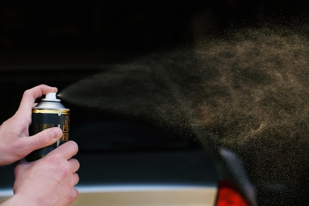 A man sprays paint from a can in front of a car