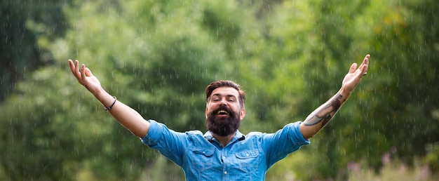 春の雨のバナーの男秋の雨の天候の概念防水着用雨の下で幸せな男