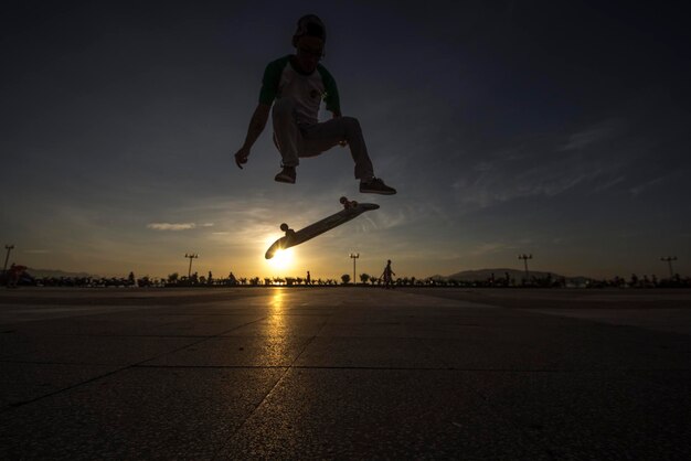 Foto man springt met skateboard tegen de hemel tijdens zonsondergang