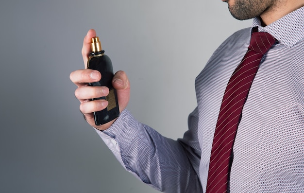 Man sprinkles perfume on gray wall .