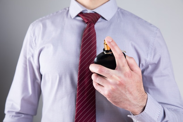 Man sprinkles perfume on gray wall .