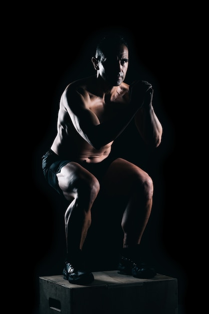 Man squatting on a box with a black background