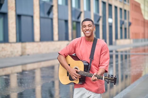 Man staande met gitaar glimlachend in de camera