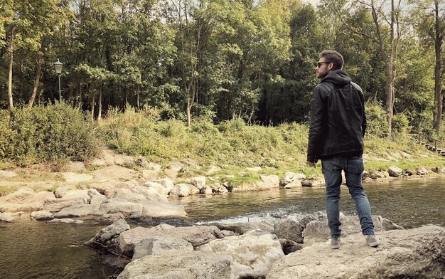 Foto man staande op een rots aan de oever van het meer tegen bomen