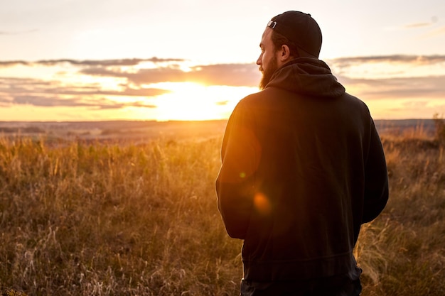 Man staat in de natuur van het platteland, ontspannend, rust na de training alleen. blanke man in zwarte sportieve kleding tijdens zonsondergang. man leidt een gezonde actieve levensstijl, sta denken, achteraanzicht