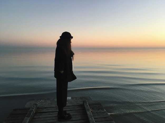 Man staat op de pier bij de zee tegen de hemel tijdens de zonsondergang