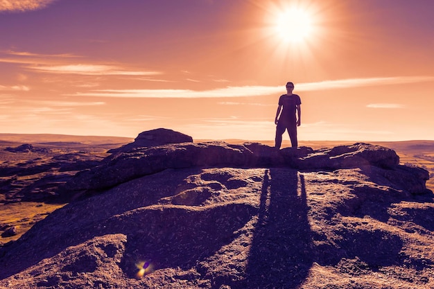 Man staat op een rots tegen de hemel bij zonsondergang